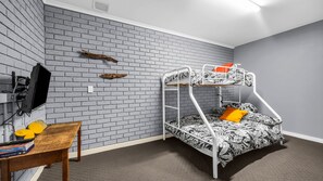 Een stapelbed met een matras met een bladmotief, een klein houten tafeltje met boeken en een aan de muur bevestigde televisie.