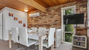 A dining area with a brick wall, white chairs, a white table, and a bookshelf with books. - Marina Townhouse 1 - Unit 1 Wapengo St 6 (BERMAGUI)