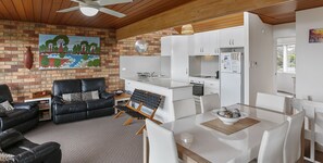 Een moderne woonkamer met een zwarte leren bank, een eettafel met witte stoelen, en een keuken met witte kasten en apparatuur.