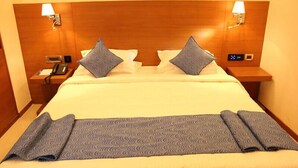 A hotel room with a large bed, two bedside tables, a nightstand, a lamp, and a control panel on the headboard. - Moskva Hotel (Madurai)