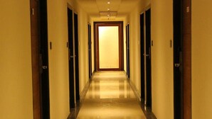 A hotel hallway with doors on both sides, a shiny floor, and a light at the end. - Moskva Hotel (Madurai)
