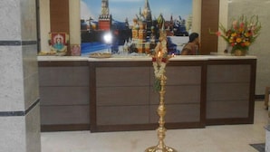 A reception area with a large painting of a cityscape, a decorative pillar, and a vase of flowers. - Moskva Hotel (Madurai)