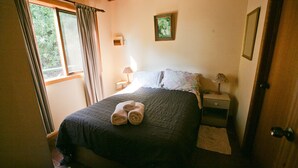 Un dormitorio con cama, dos lámparas de noche, una ventana con cortinas, un cuadro en la pared y una puerta.