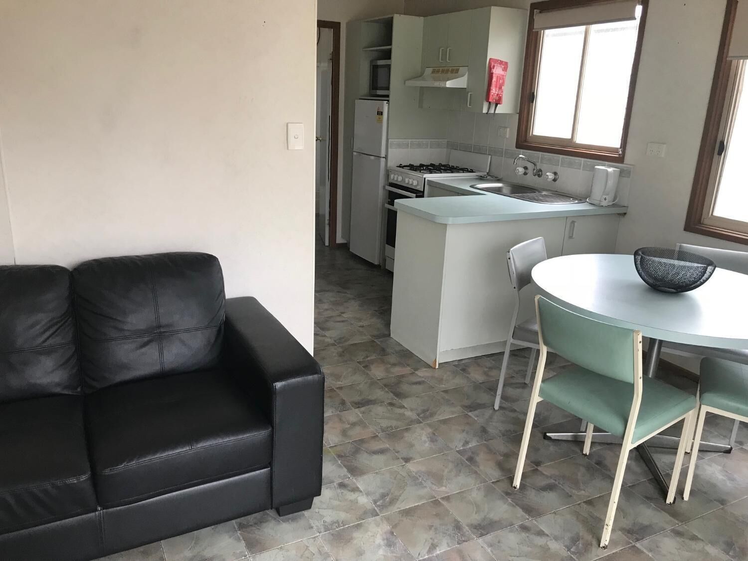 A compact living space with a kitchenette, a dining area with a table and chairs, and a black leather sofa.