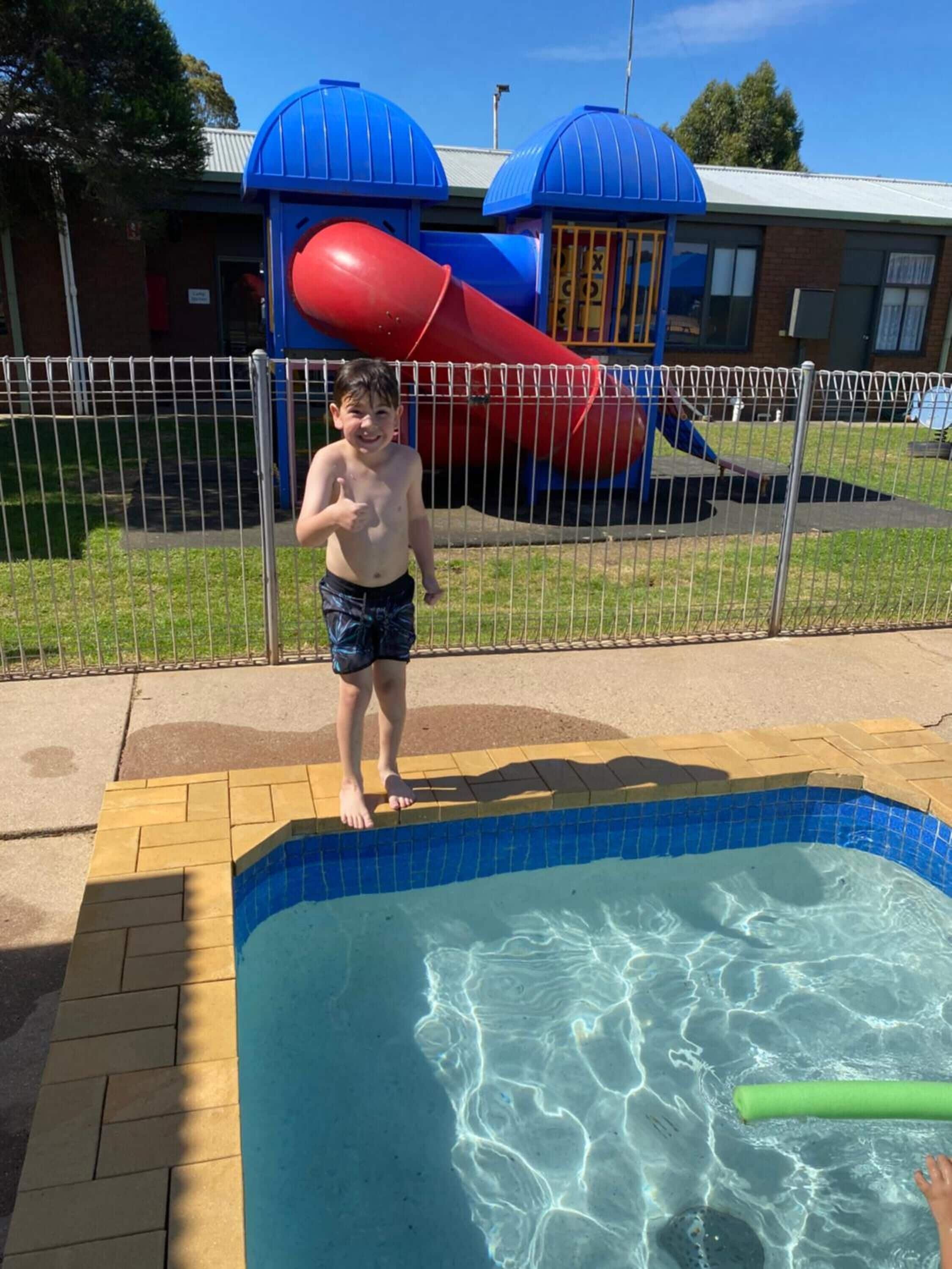 Un niño de pie junto a una piscina con un tobogán al fondo.