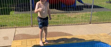 Un niño de pie junto a una piscina con un tobogán al fondo.