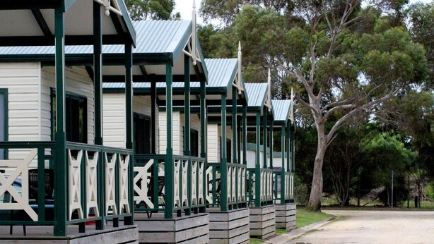 Une rangée de cabanes en bois, dotées de balustrades vertes et de toits en métal, entourées d’arbres.