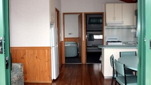 Une cuisine compacte équipée d’un réfrigérateur, d’une cuisinière et de meubles de rangement en bois. On y trouve également un petit coin repas avec une table et des chaises.