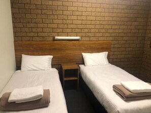 Une chambre d’hôtel avec deux lits simples, chacun doté de draps et d’oreillers blancs, d’une tête de lit en bois et d’une petite table de chevet.