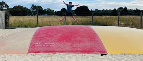 Une personne saute sur un trampoline près d’une plage, à proximité d’un panneau d’avertissement indiquant : « IL EST INTERDIT DE SAUTER PRÈS DU BORD ».