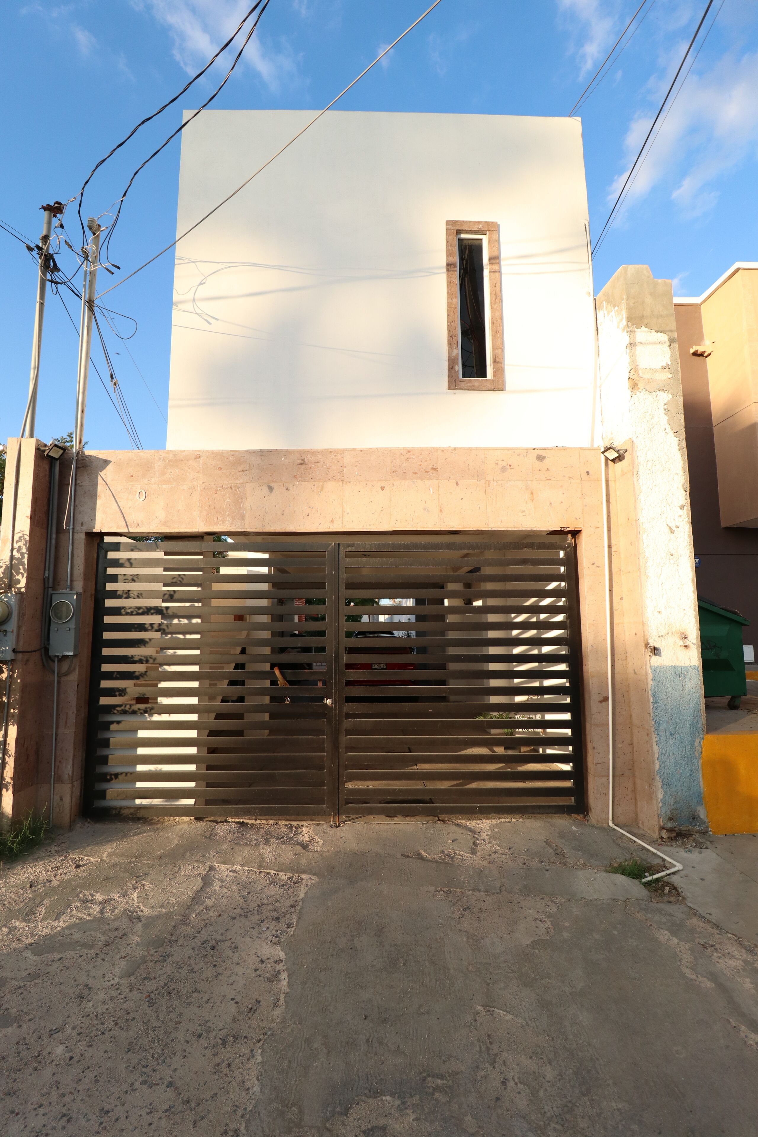 Un edificio con un gran portón metálico, una ventana pequeña y suelo de hormigón.
