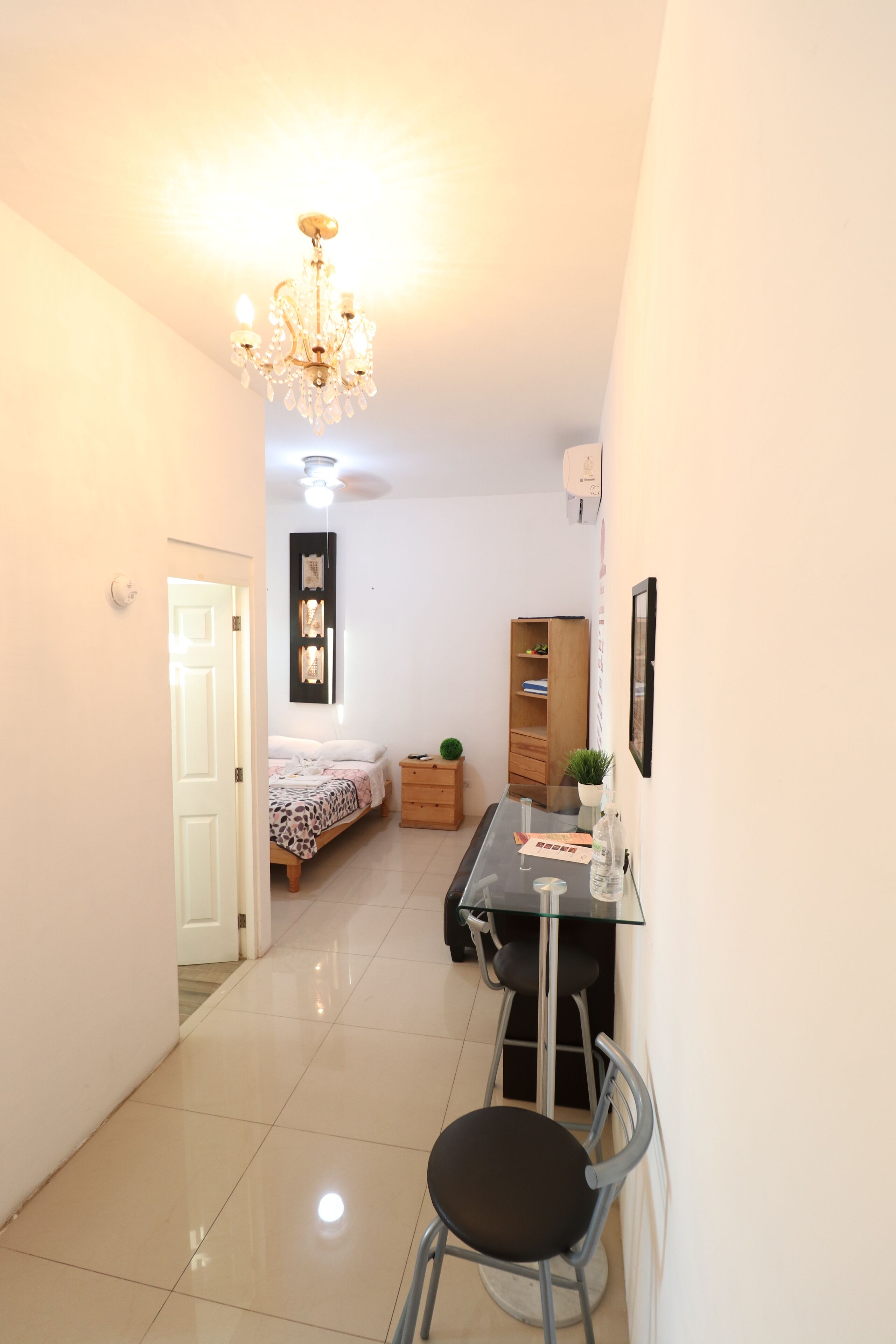 A hallway leading to a bedroom with a bed, a dresser, and a desk with a chair.