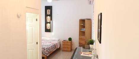 A hallway leading to a bedroom with a bed, a dresser, and a desk with a chair.