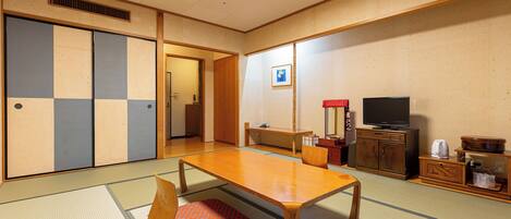 Una habitación japonesa tradicional con suelo de tatami, una mesa de madera baja, un televisor y una puerta corredera.