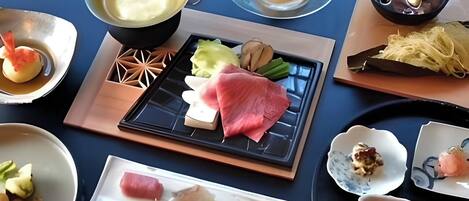 Una mesa de comedor con diversos platos, como sashimi, verduras y una olla de sopa.