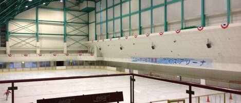 An indoor ice rink with benches along the side, a high ceiling with green beams, and a sign in a foreign language.