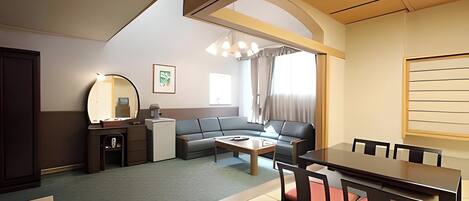 A hotel room with a sofa, a dining table, a desk, and a mirror.