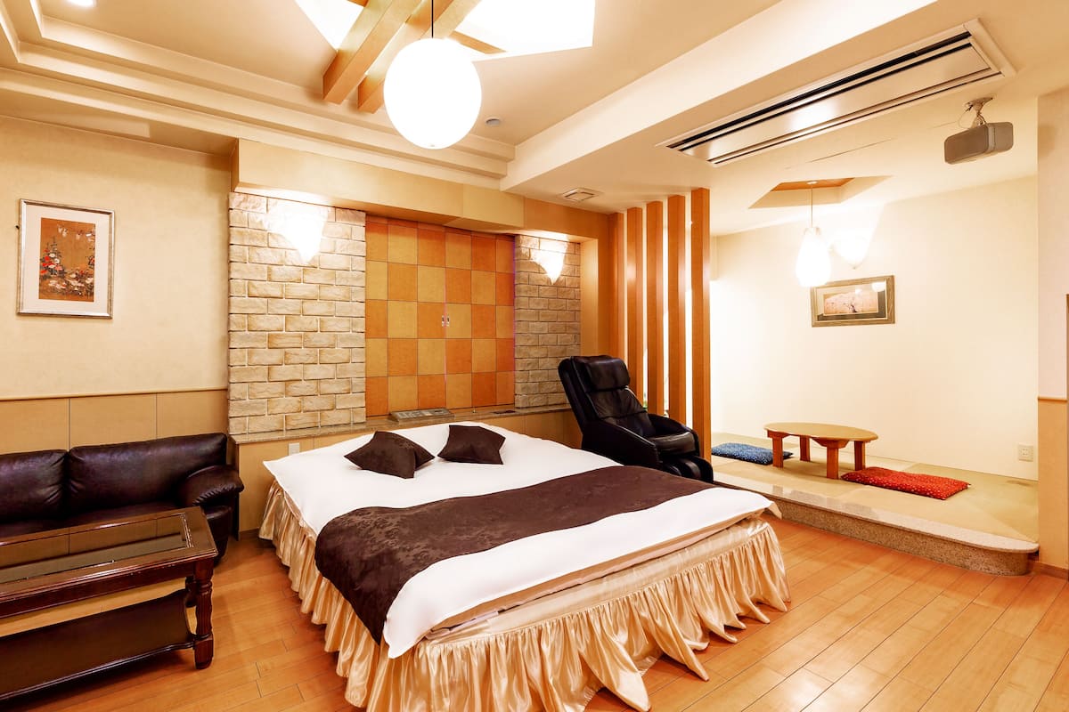 A hotel room with a large bed, a massage chair, a small table, and a sofa.