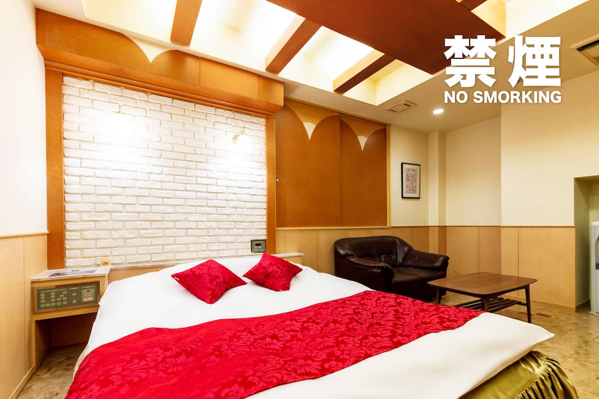 A hotel room with a bed, a chair, a small table, and a wall with a no smoking sign.