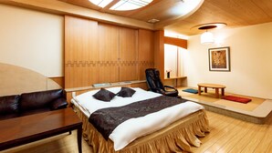 Une chambre d’hôtel avec un lit, un bureau, une chaise, une petite table et une lucarne ronde.