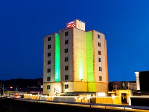 Un hotel a più piani con un cartello ben visibile che indica il nome. L'edificio presenta una fascia verticale di illuminazione verde su un lato.