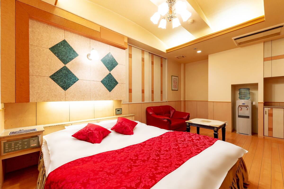 A hotel room with a bed, a red chair, a water dispenser, and a small table.