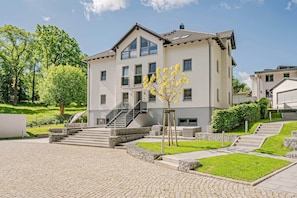 A modern two-story building with a staircase leading to the entrance, surrounded by a well-maintained lawn and stone pathways.