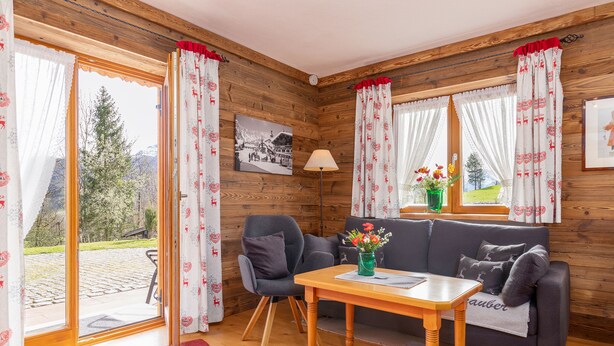 A cozy room with a wooden interior, a sofa, a table, and a window with curtains. - Ferienwohnung (09) im Birkenhof (Reit im Winkl)