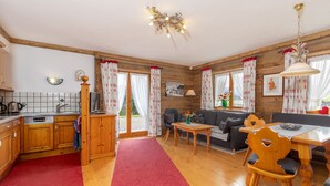 A cozy kitchen with wooden cabinets, a dining area with a table and chairs, and a living room with a sofa and a fireplace. - Ferienwohnung (09) im Birkenhof (Reit im Winkl)