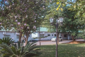 A building with a green roof, surrounded by trees and a white car parked in front. - Acamms Lodge Roma (Lusaka)