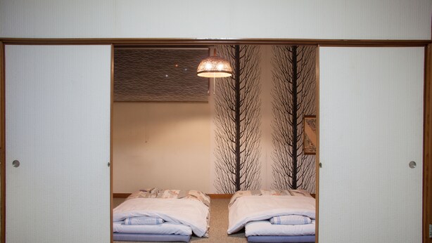 Una habitación con dos camas, una lámpara colgante y un papel tapiz con estampado de árboles.