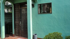 Un edificio con fachada azul verdosa, una puerta marrón oscuro con diseños intrincados y un ventanal pequeño.