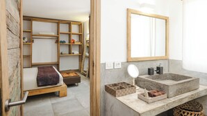 Quarto compacto com cama, guarda-roupa de madeira, estante embutida, pia de pedra e espelho.