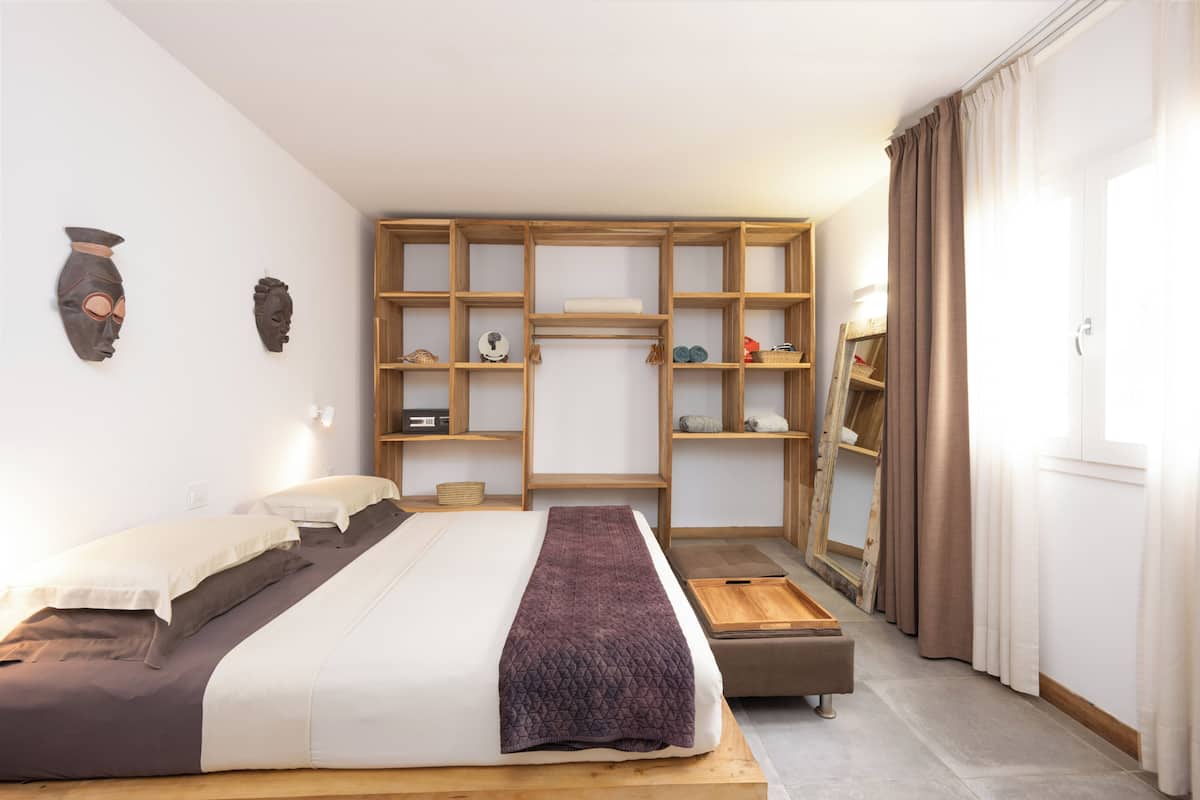 Un dormitorio con una cama, una estantería de madera, un pequeño banco y un armario.