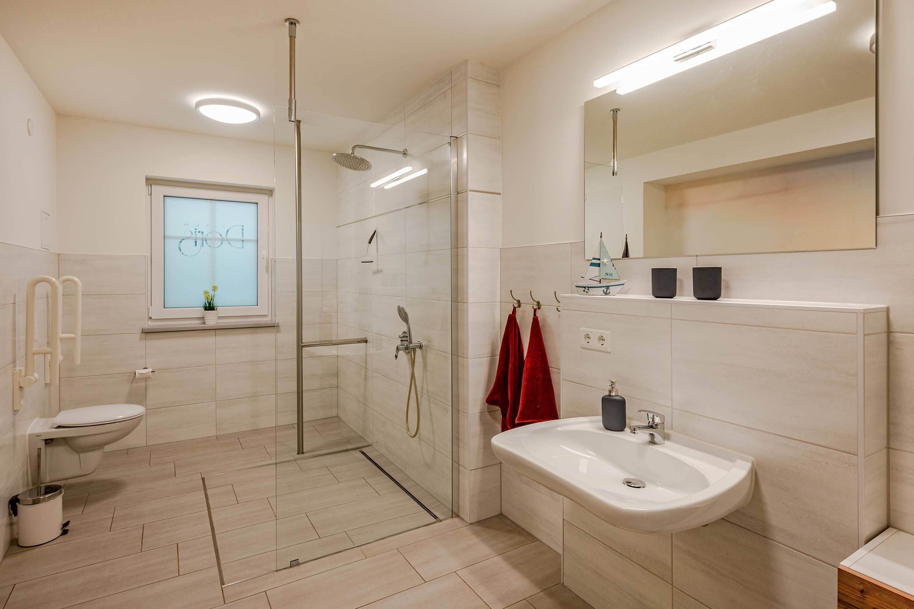 Une salle de bain moderne équipée d’une douche, de toilettes et d’un lavabo, avec un grand miroir et une fenêtre.