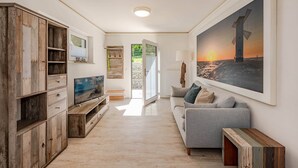 Una sala de estar moderna con un mueble de madera, un sofá gris, un cuadro de un faro y un televisor.