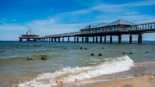Un muelle que se adentra en el agua, con un edificio al final, sostenido por varios pilares.