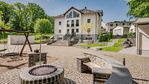 Una casa moderna con un patio que incluye un columpio, una fogata y un banco de piedra.