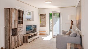Un salón con un sofá gris, un aparador de madera, televisor y una puerta que da al exterior.