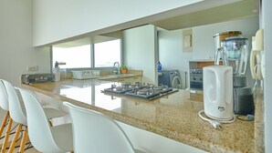 Une cuisine moderne dotée d’un plan de travail en granit, de chaises blanches, d’une cuisinière encastrée et d’une machine à café.