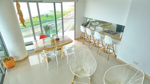 Une cuisine moderne avec des meubles blancs, un plan de travail en bois et une vue sur une route, visible à travers de grandes fenêtres.