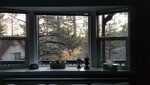 A bay window with three panes, a potted plant, and two candle holders on the windowsill.