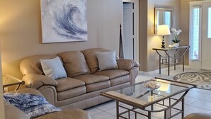 Un salon avec un canapé beige, une table basse en verre et un grand tableau abstrait accroché au mur.