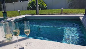 Une piscine à l’eau d’un bleu cristallin, entourée d’une terrasse blanche. On y trouve deux verres à vin vides et une bouteille de vin.