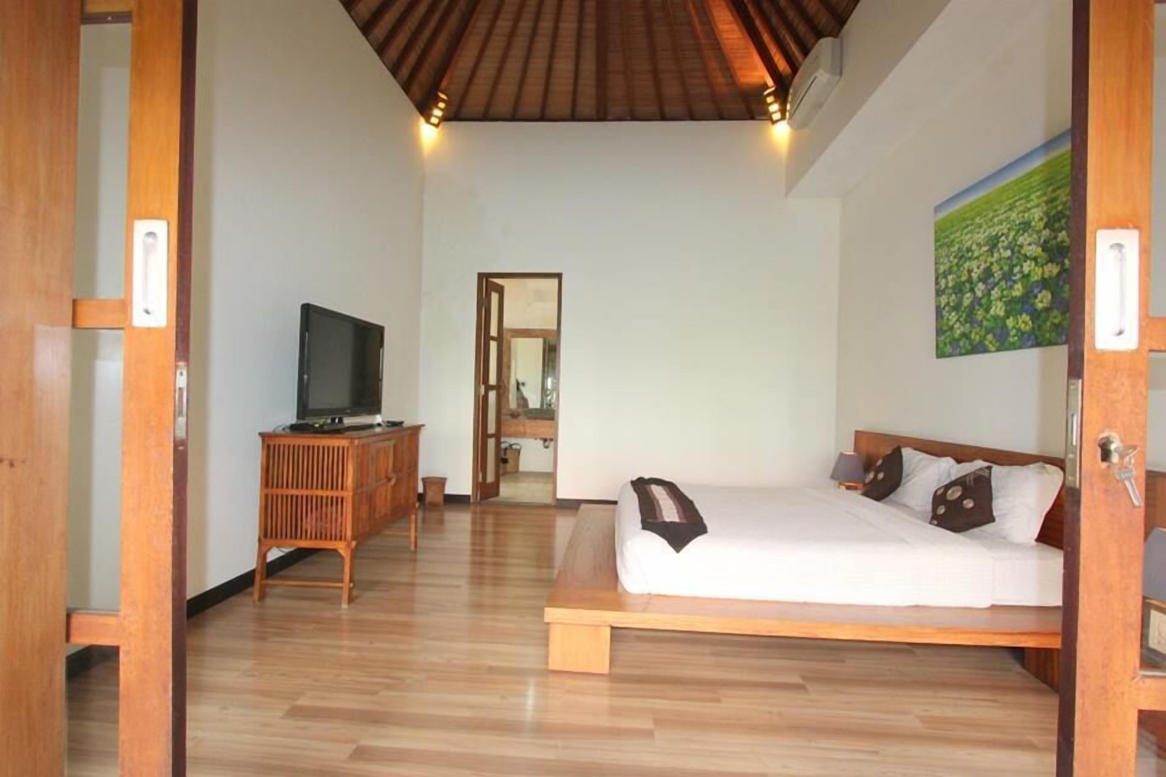 A bedroom with a wooden bed, a television on a wooden cabinet, and a painting on the wall.