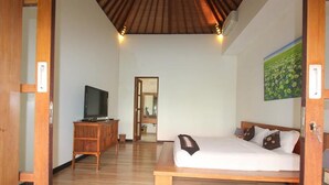 A bedroom with a wooden bed, a television on a wooden cabinet, and a painting on the wall. - Villa Anya Seminyak (Seminyak)