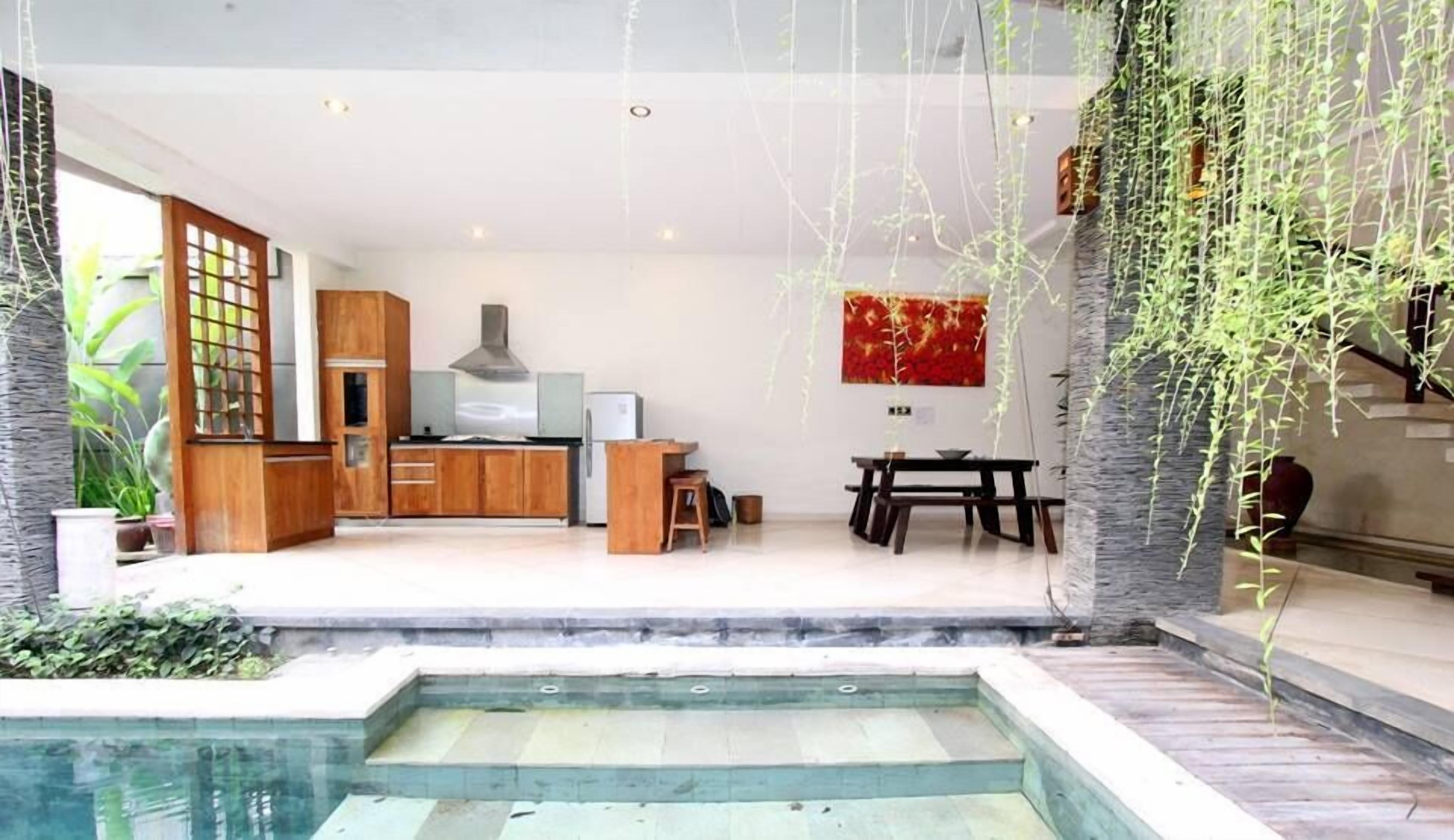Uma cozinha moderna com armários de madeira, fogão a gás e um espaço de refeições com mesa e cadeiras. Há uma pequena piscina em primeiro plano.
