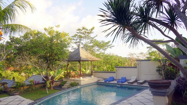 A swimming pool with lounge chairs and a gazebo surrounded by lush greenery. - Villa Annapurna Bali (Mengwi)