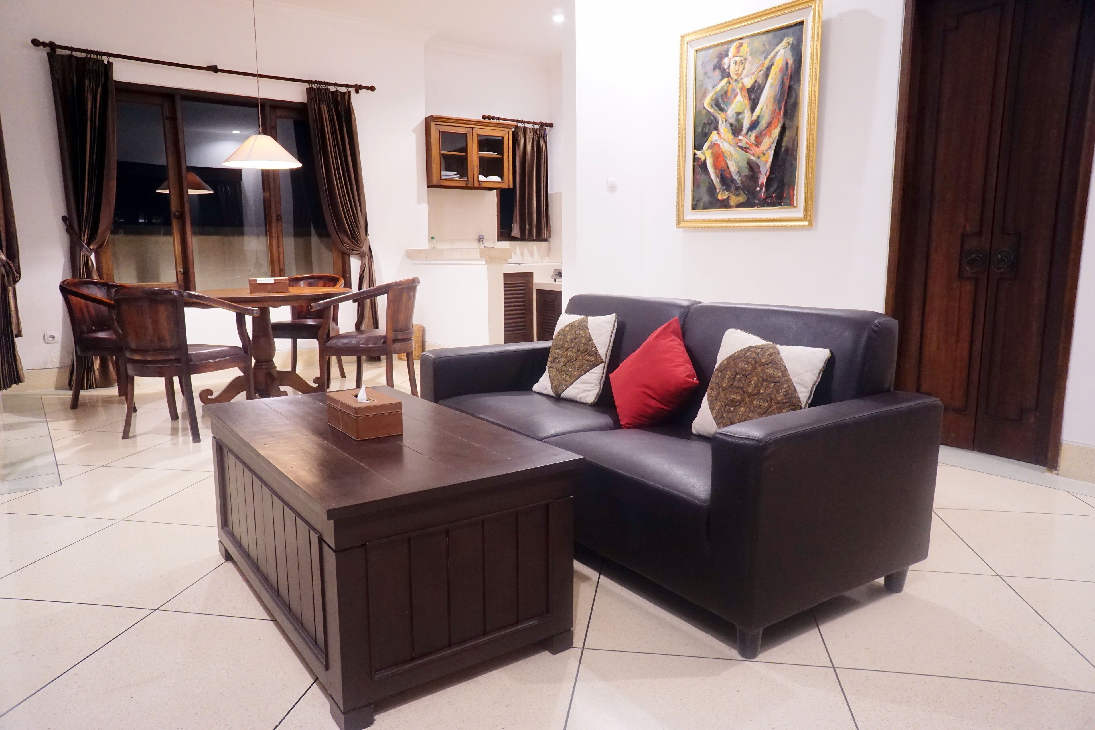 Una sala de estar con un sofá de color oscuro, una mesa de centro de madera, una mesa de comedor con sillas y una zona de cocina al fondo.