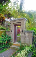 Un portón de piedra con puerta de madera, rodeado de abundante vegetación y plantas.